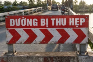Biển báo đường hẹp chữ ĐƯỜNG BỊ THU HẸP nền đỏ, dải mũi tên đỏ trắng, gắn trên hai trụ thép ở đầu cầu