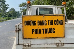 Biển nền vàng chữ đen Đường đang thi công phía trước gắn sau thùng xe tải trên đường nhựa