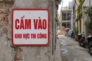 Biển vuông nền trắng viền đỏ, chữ đỏ Cấm vào Khu vực thi công, bắt vít trên tường gạch ở đầu hẻm có công trình đang xây phía xa