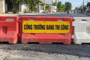 Biển nền vàng chữ đen Công trường đang thi công gắn lên dãy rào nhựa đỏ trắng chắn ngang mặt đường đang sửa