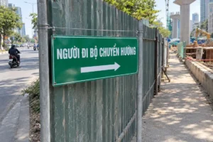 Biển nền xanh lục chữ trắng Người đi bộ chuyển hướng, mũi tên sang phải, gắn trên hàng rào tôn cạnh vỉa hè thi công