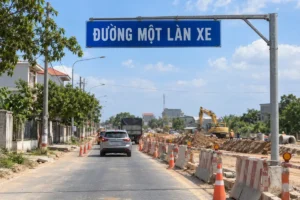 Bảng xanh chữ trắng Đường một làn xe treo ngang trên cần thép phía trên đường đang sửa, có nón và rào đỏ trắng