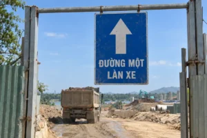 Bảng xanh mũi tên trắng chỉ lên và chữ Đường một làn xe, treo trên khung ngang ở lối vào công trường, xe tải phía sau