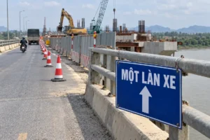 Bảng xanh chữ Một làn xe kèm mũi tên trắng chỉ lên, gắn vào lan can thép cạnh đoạn cầu đang thi công