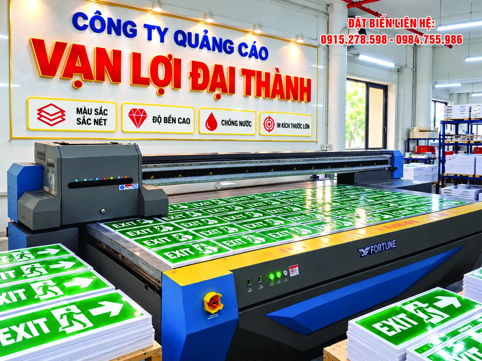 Máy in UV phẳng đang in lô biển chỉ dẫn lối thoát EXIT, bên cạnh là các biển đã in